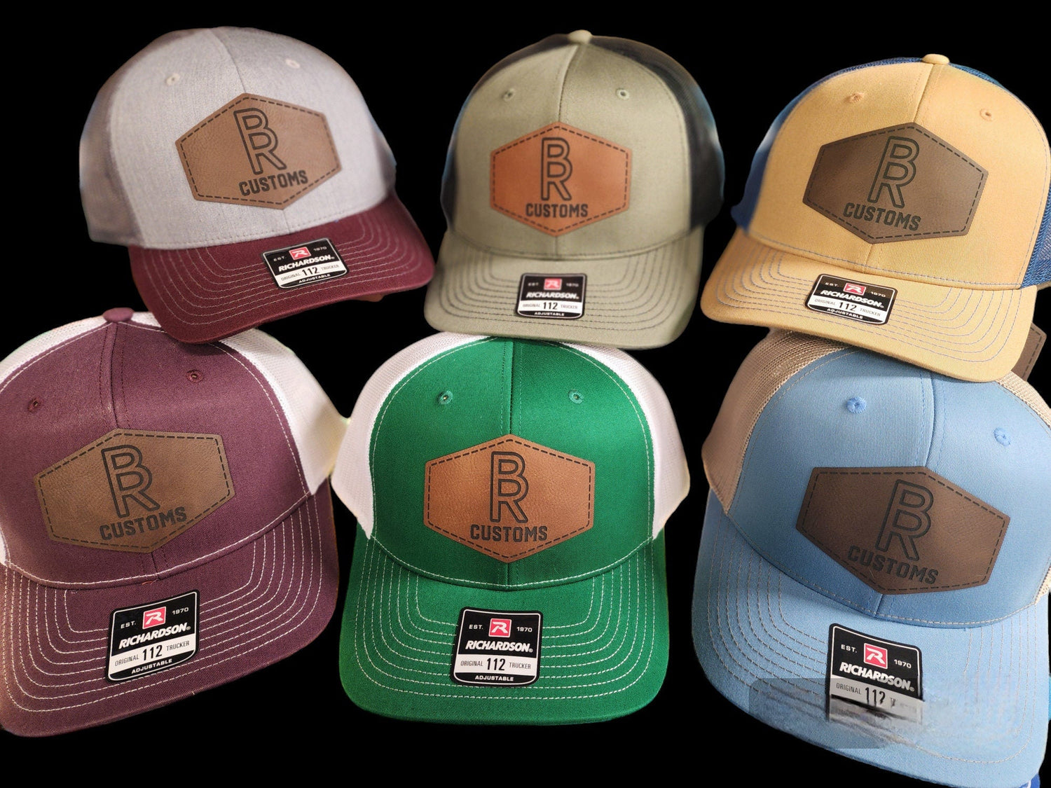 Collection of custom engraved hats in various colors featuring brown leather patches with logo and text